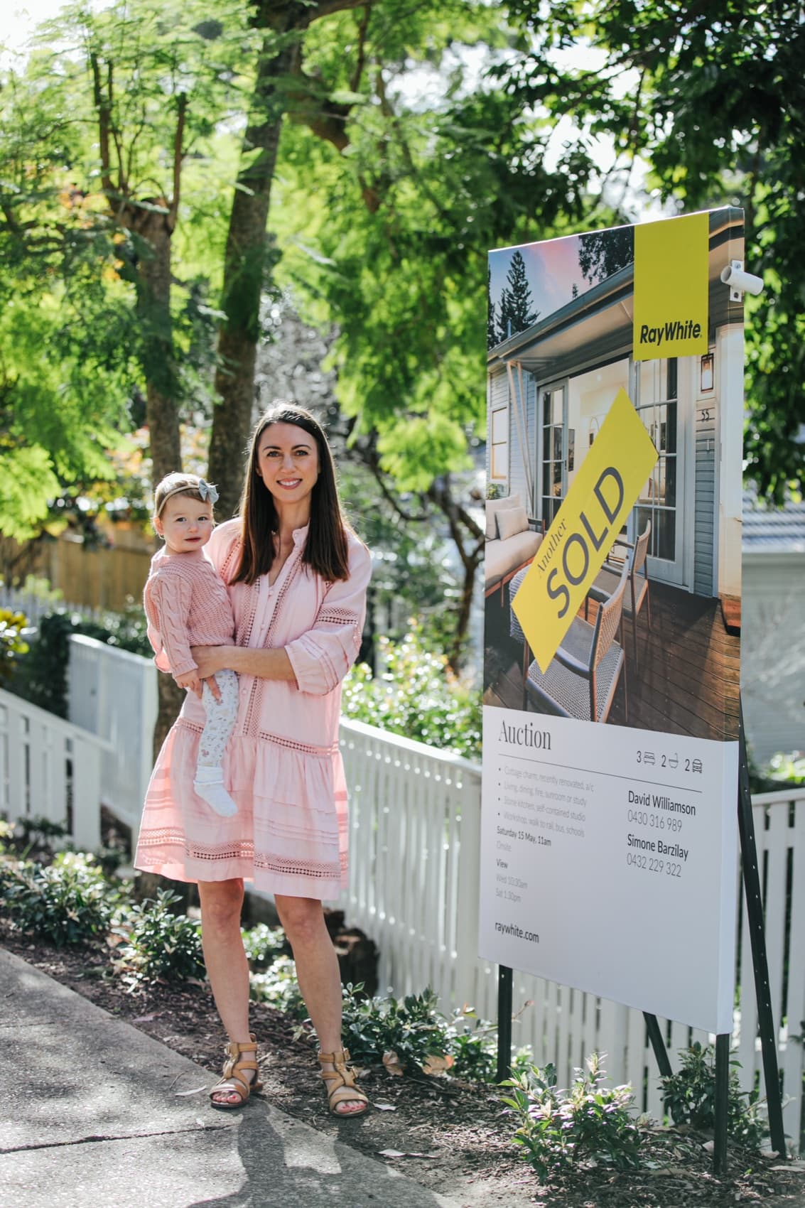 A mother and daughter outside their home beside a Ray White sold sign