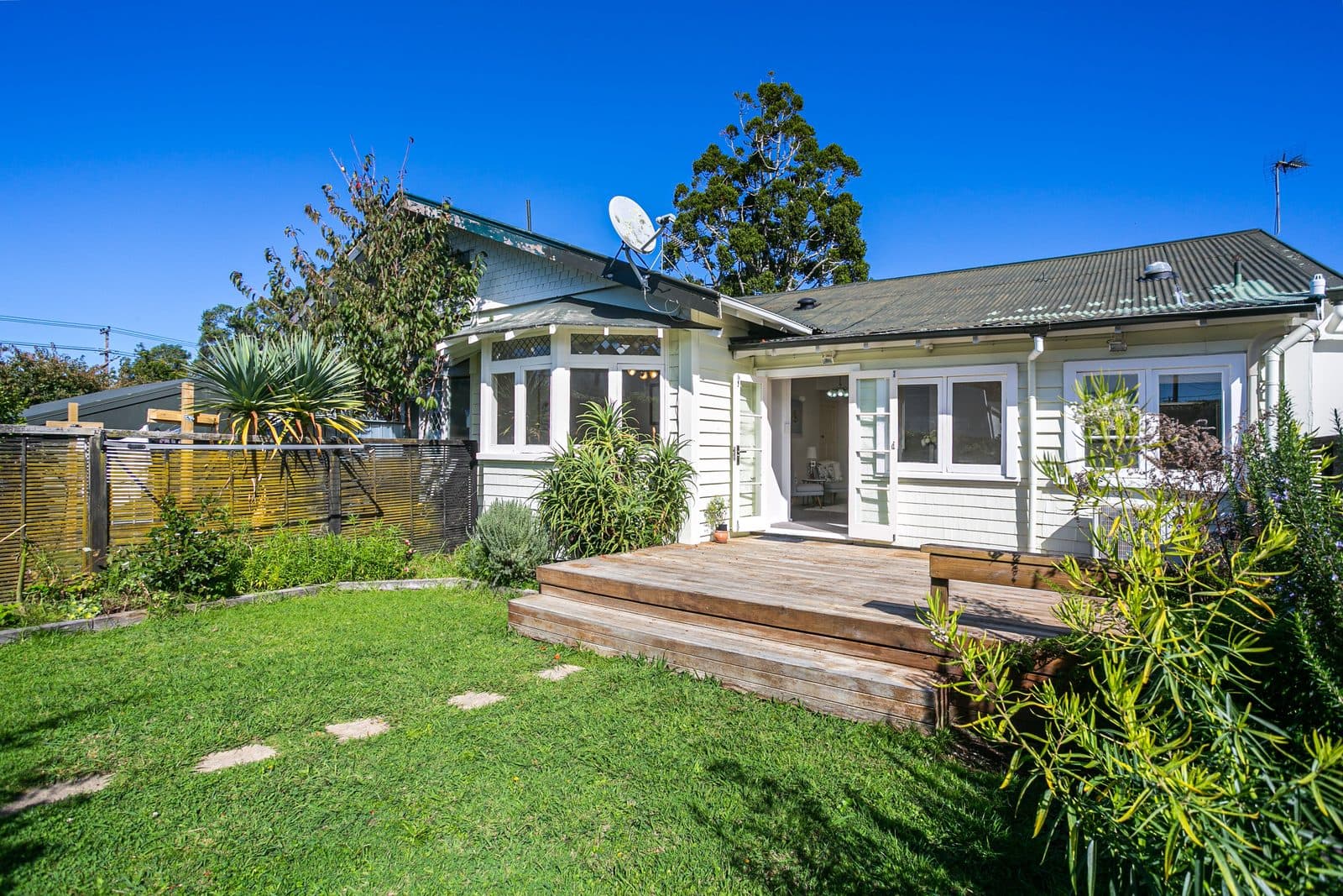 A white weatherboard bungalow with a timber deck in an Onehunga garden