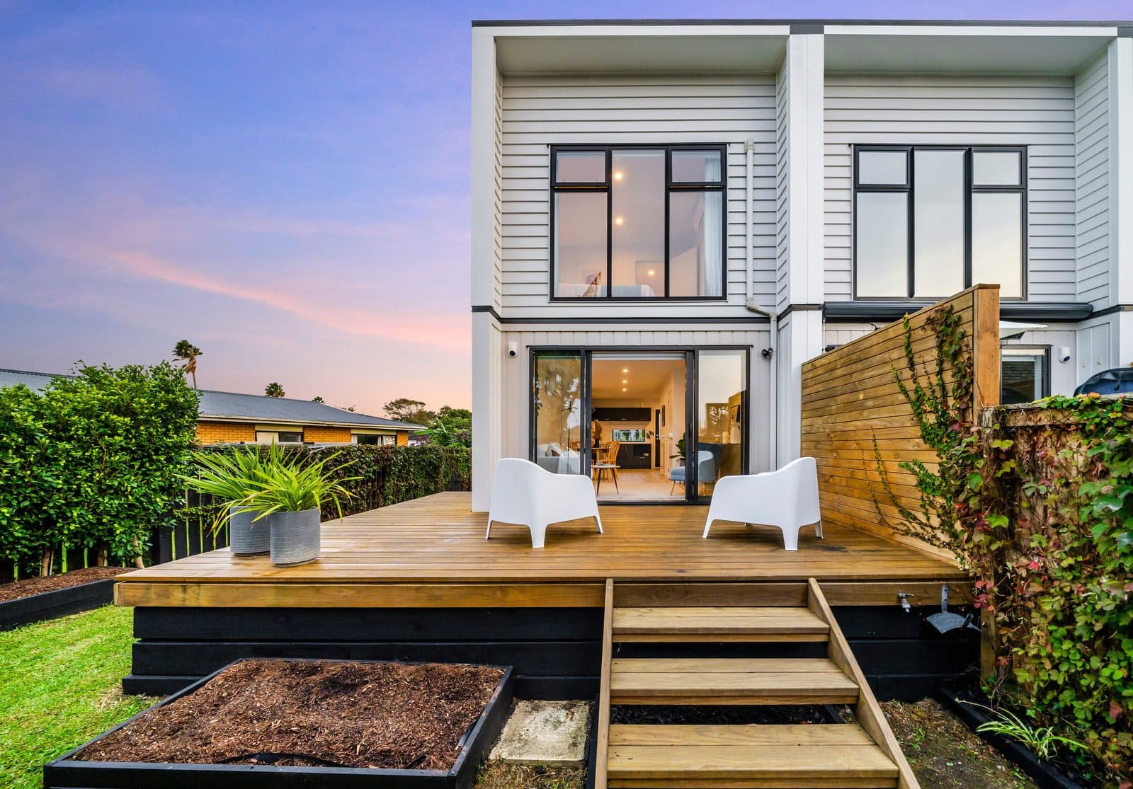 A new two-storey townhouse with a timber deck, photographed at dusk in Panmure