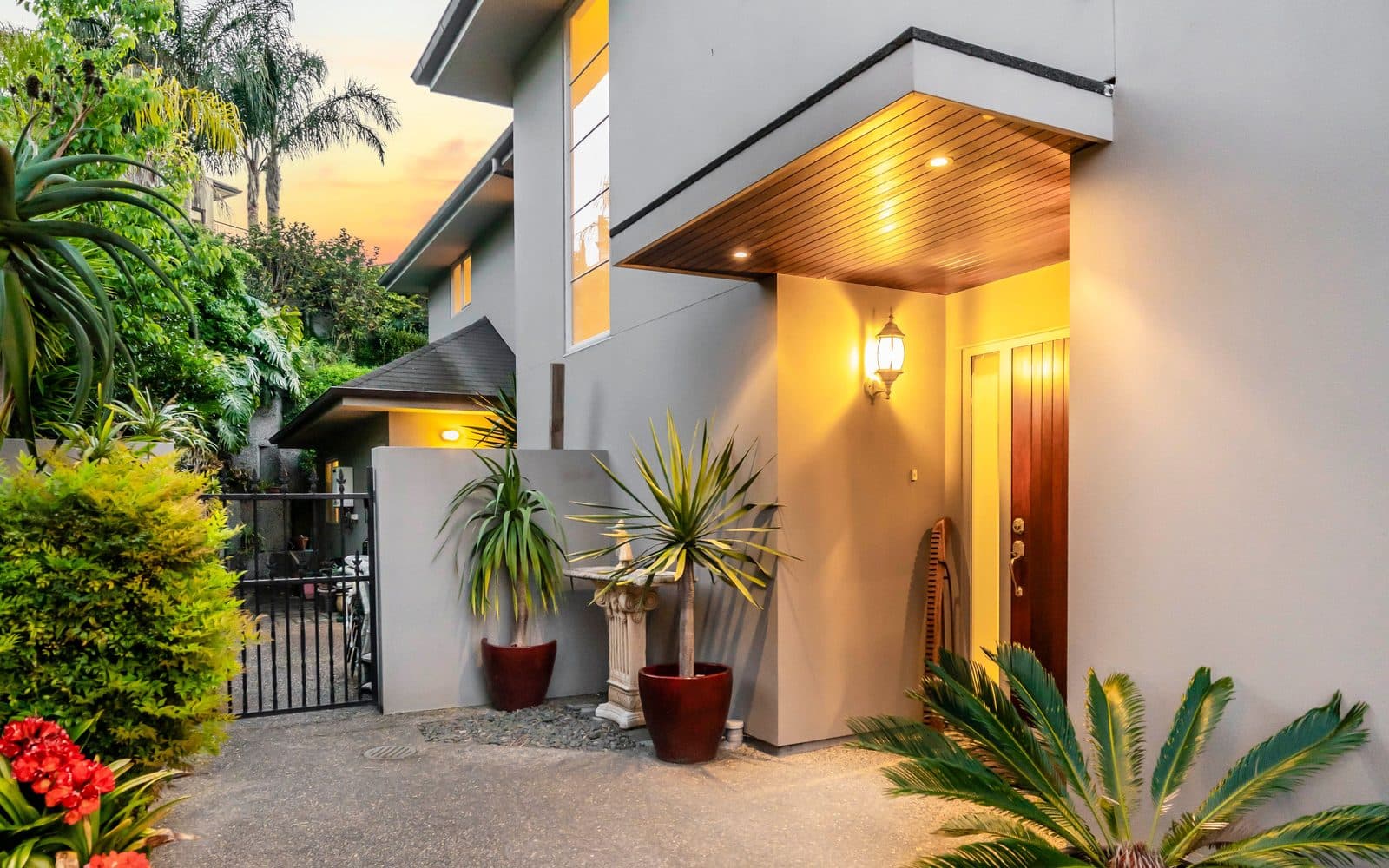 The lit entrance of a substantial family home in Remuera at dusk, framed by palms