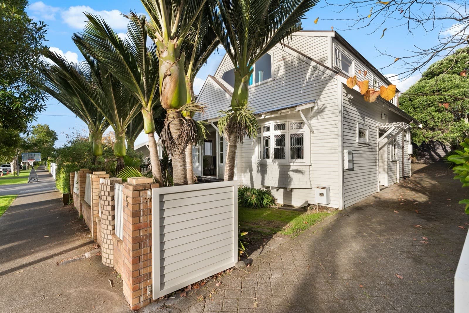 A white weatherboard character home behind nikau palms on a Westmere street