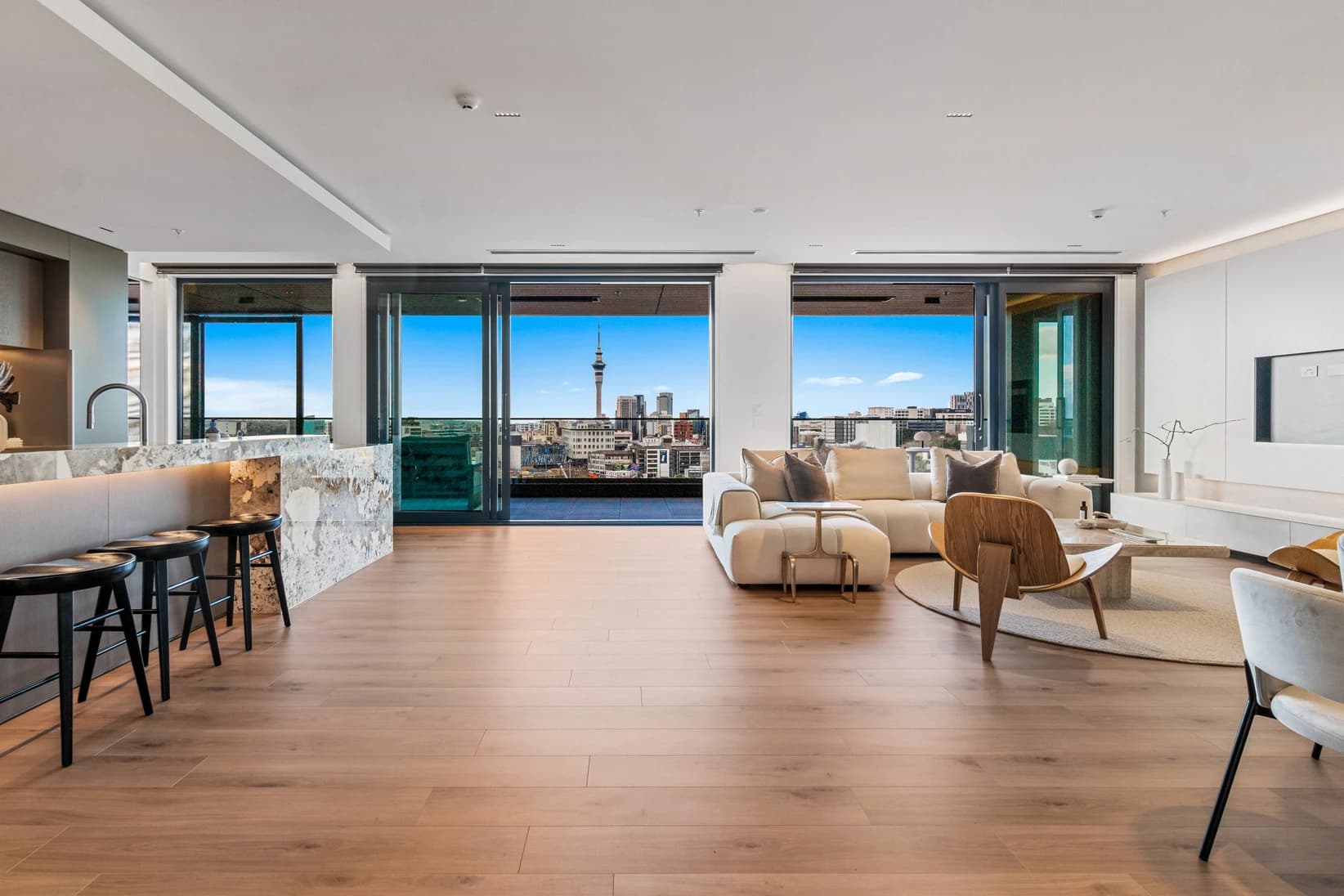 Open-plan apartment living area with Sky Tower views through floor-to-ceiling windows, marble island and timber floors