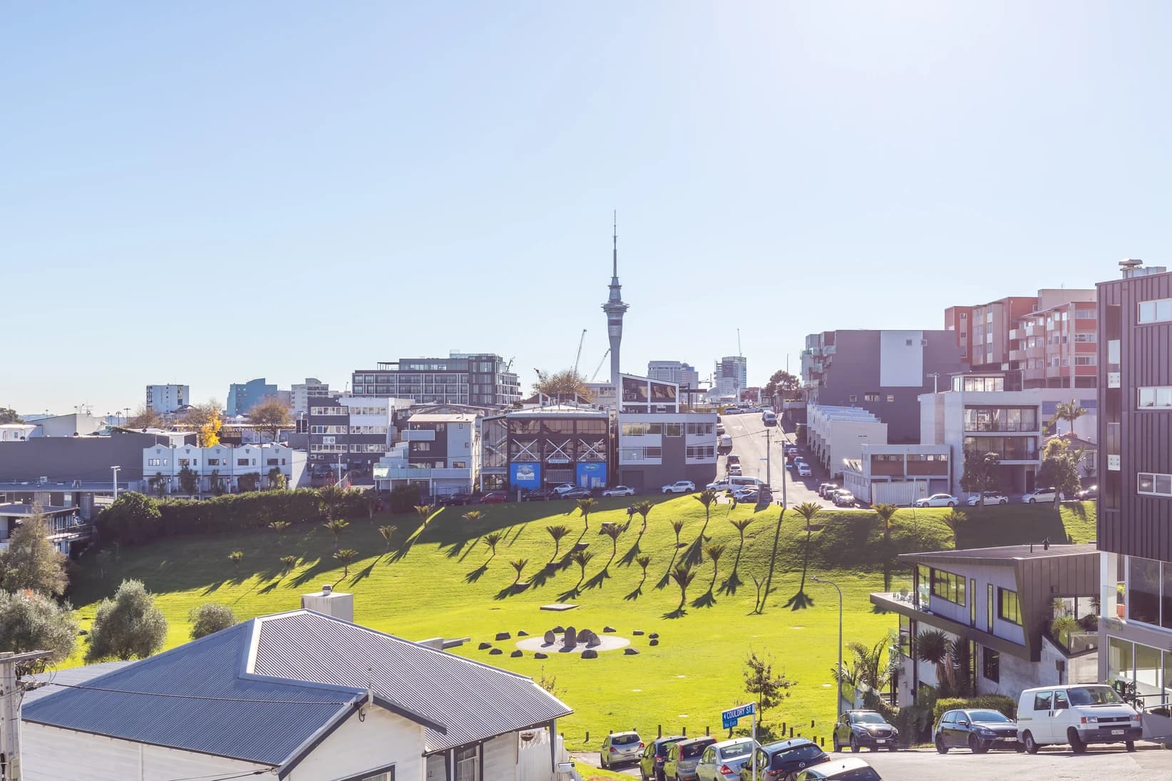 Eden Terrace neighbourhood view across Basque Park towards the Sky Tower and city centre with palm trees and mixed-use buildings